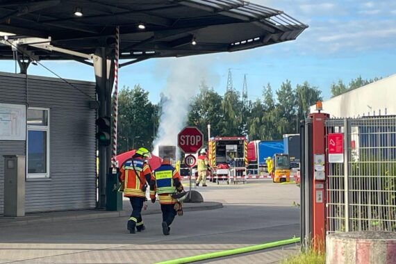 Feuerwehr löscht qualmende Wechselbrücke; Einsatzkräfte in Schutzanzügen, Rauchentwicklung sichtbar.