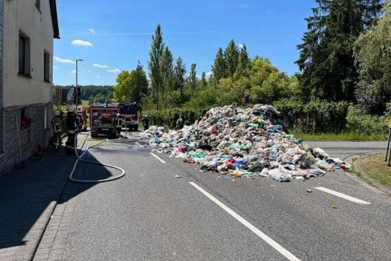 Brennender Müllcontainer auf Straße, Feuerwehr löscht, illegale Akkus als Brandursache vermutet.