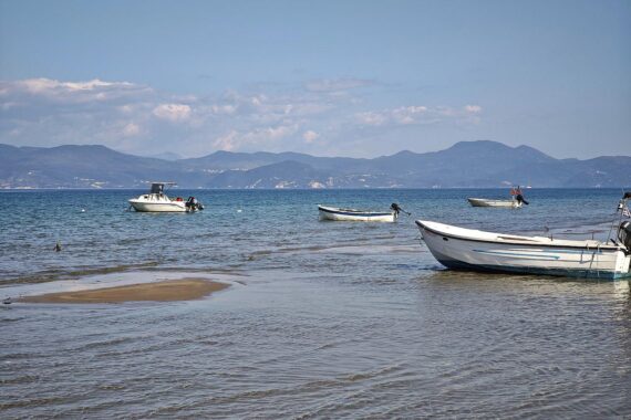 Boote am Strand von Korfu symbolisieren Reisemöglichkeiten, die für viele unerschwinglich bleiben.