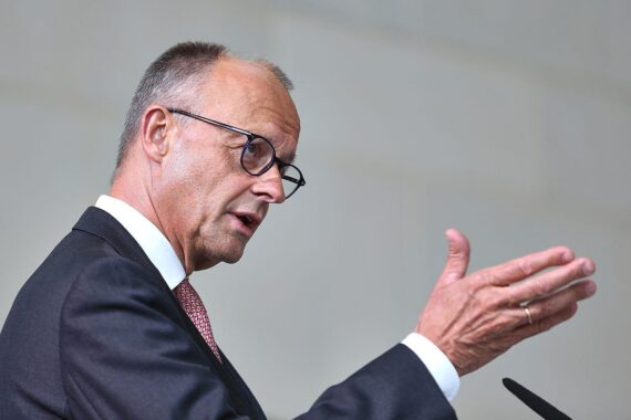 Friedrich Merz spricht vor Publikum, umgeben von technologischen Symbolen und KI-Diskussionen.