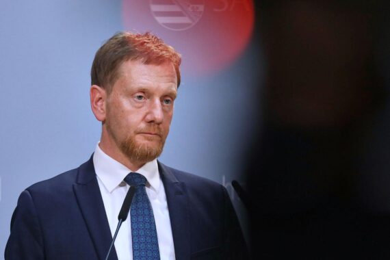 Michael Kretschmer warnt vor der Gefahr der AfD, symbolisiert durch eine Brandmauer.