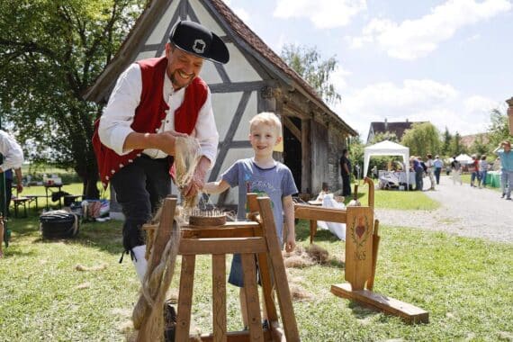 Kinder und Erwachsene erlernen traditionelle Flachsverarbeitung im historischen Oberschwäbischen Museumsdorf.