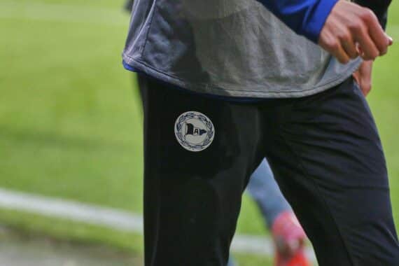 Oliver Kirch in Bielefelds Trainerjacke, begeistert im Stadionumfeld, symbolisiert Neuanfang und Teamgeist.
