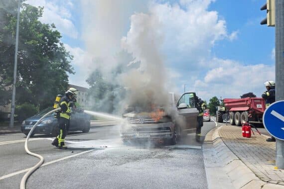 Feuerwehr löscht brennenden Pkw; Einsatzkräfte und umliegende Unternehmen unterstützen löschen.