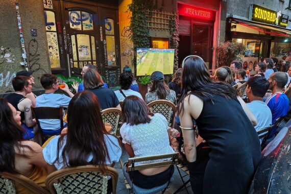 Menschen verfolgen gemeinsam ein Fußballspiel auf der Straße, begeistert und interaktiv.