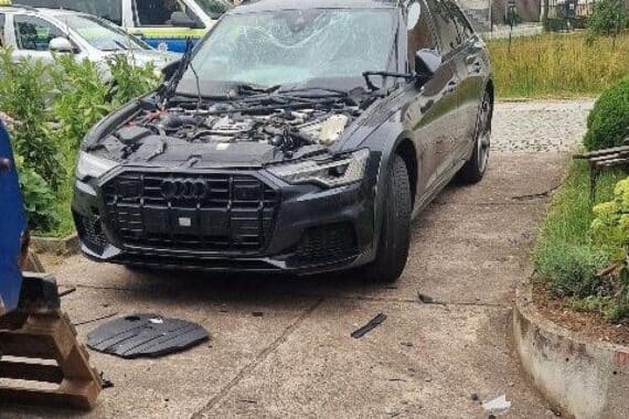 Zerstörter Audi A6 nach Sprengstoffanschlag; Motorhaube abgerissen, schwere Schäden sichtbar.