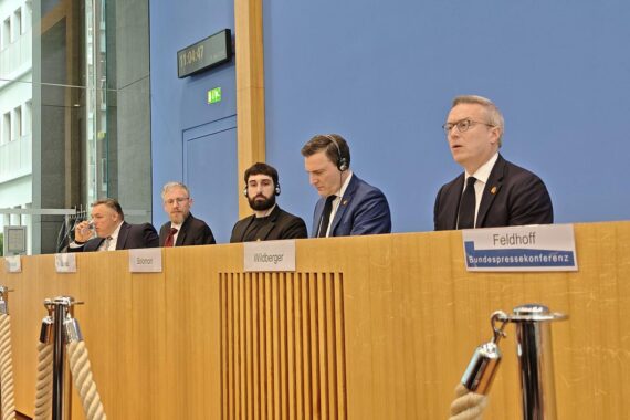 Pressekonferenz zur deutsch-kanadischen KI-Partnerschaft, symbolisiert durch Redner, Grafiken und Technik.