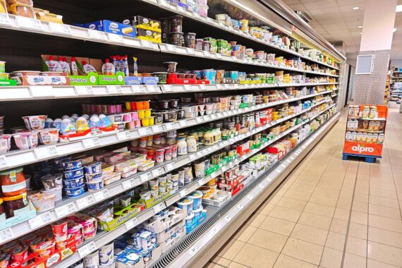 Supermarkt-Regal, Käufer im Bild; Schild „Preise steigen“ deutet höhere Inflation und gestiegene Kraftstoffkosten an.