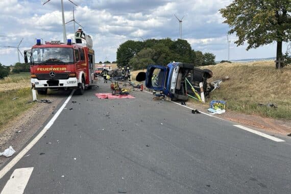 Unfallstelle auf der L 9: umgestürzter Pritschenwagen auf dem Dach, Rettungskräfte und Verletzte.