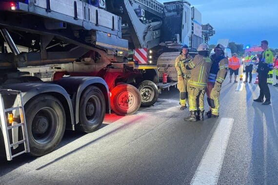 Einsatzkräfte löschen Brand am Schwertransporter unter Autobahnbrücke, Feuerwehr kontrolliert mit Wärmebildkamera.