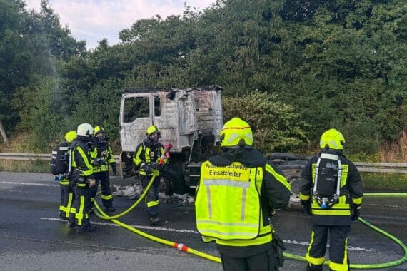 Feuerwehr löscht Lkw-Brand auf der Autobahn A1; Zugmaschine in Vollbrand, Einsatzfahrzeuge und Blaulicht.