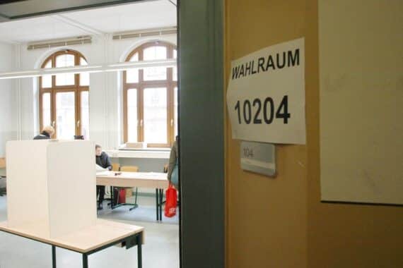 Politikwissenschaftler kritisiert Sperrklausel; im Hintergrund: Wahllokal (Archiv) mit Wahlurne/Stimmzetteln.
