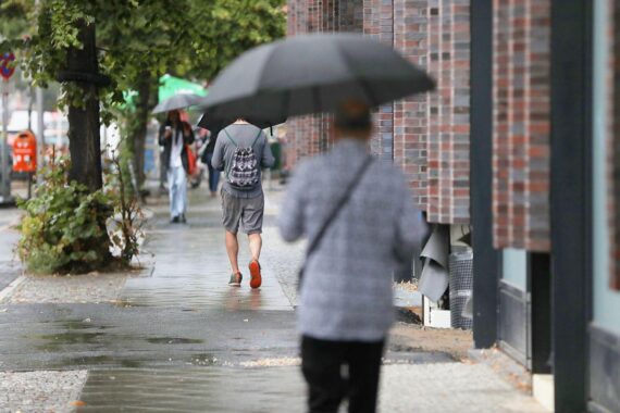 Passanten mit Regenschirmen bei überwiegend bewölktem Wetter, vereinzelte Schauer und mögliche Gewitter.