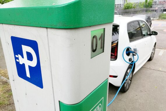 E-Auto-Ladestation (Archiv) vor industriellem Hintergrund; Diskussion über Tempo beim Batteriebau in Europa.