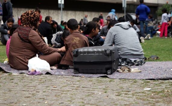 Flüchtlinge an einer Aufnahmestelle (Archiv), im Hintergrund deutsche EU-Abschiebung nach Ruanda.