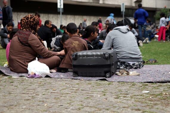 Flüchtlinge an einer Aufnahmestelle (Archiv), im Hintergrund deutsche EU-Abschiebung nach Ruanda.
