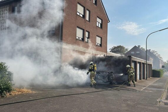 Feuerwehr im Einsatz: Vollbrand eines Elektroautos neben Mehrfamilienhaus; Gebäude evakuiert, Glutnester geprüft.