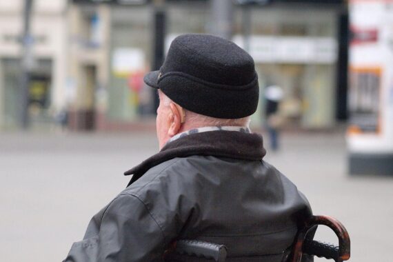 Mann im Rollstuhl (Archiv) vor Parlamentskulisse, Gewerkschaftskritik an Renten-Aus „Rente mit 63“.