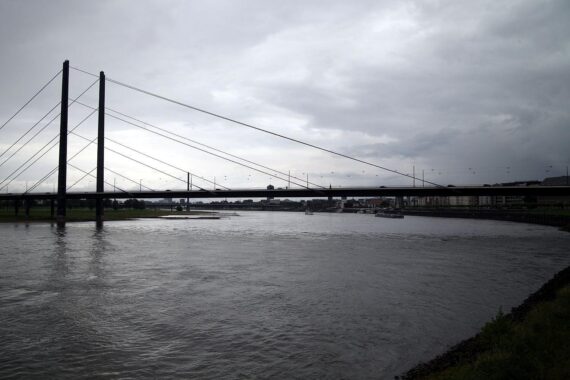 Rhein bei Düsseldorf: Rheinkniebrücke über Niedrigwasser, warnendes Schlagzeilenmotiv zur Gefahr für Gütertransporte.