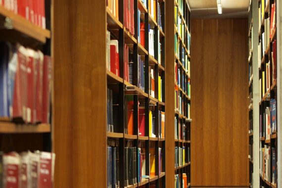 Bücher in einer Bibliothek (Archiv); Artikel über strengere Regeln für Hochschulen, KI, Drohnenforschung und Cybersicherheit.