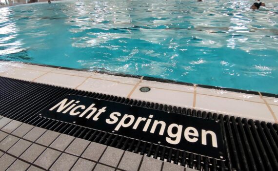 Schwimmbad (Archiv): Eltern mit Smartphone im Freibad, um Warnung vor Badeunfällen und Personalmangel zu verdeutlichen.