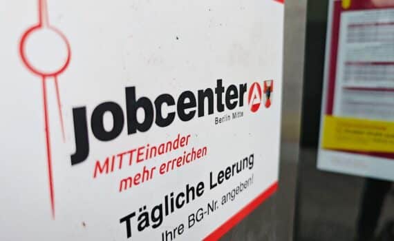 Jobcenter-Archivfoto: Menschen und Schalter, im Hintergrund ein Verwaltungsgebäude.