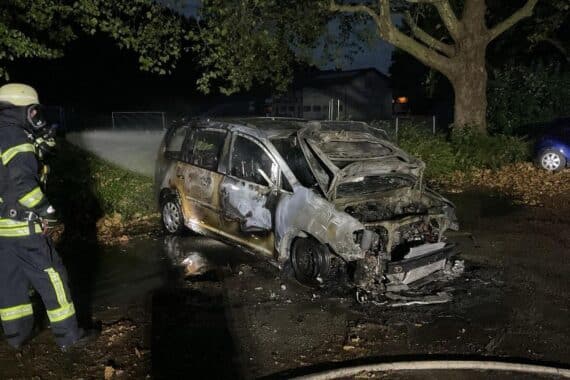 Feuerwehr löscht einen vollständig zerstörten VW-Minivanbrand auf Parkplatz neben Sportplatz in Zunsweier.