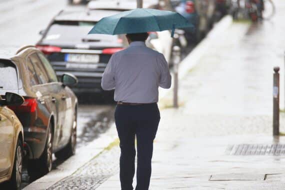 Mann mit Regenschirm bei überwiegend bewölktem Himmel, mögliche Gewitter und Schauer in Hamburg/Schleswig-Holstein.
