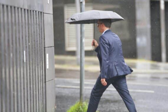 Mann mit Regenschirm im Regenwetter, stark bewölkt mit Schauern und Gewittern in Thüringen.