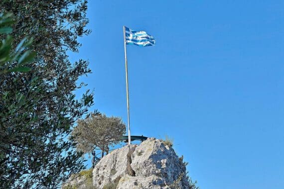 Griechische Flagge im Hintergrund, dazu Rettungseinsatz/Feuerwehr-Hubschrauber nach Waldbränden in Athen.