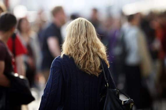 Blonde Frau mit Locken vor Bankgebäude: Kreditvergabe für Frauen oft teurer, kleinere Beträge, häufiger abgelehnt.