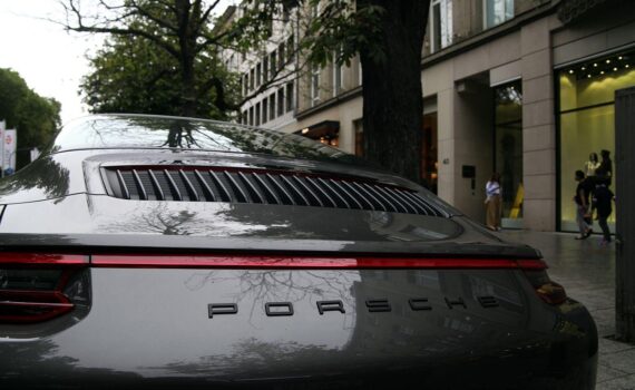 Porsche-Auto vor Düsseldorfer Kö (Archiv), im Hintergrund VW-Sparmaßnahmen durch Gewinnwarnung angedeutet.