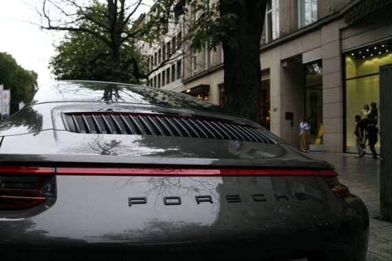 Porsche-Auto vor Düsseldorfer Kö (Archiv), im Hintergrund VW-Sparmaßnahmen durch Gewinnwarnung angedeutet.