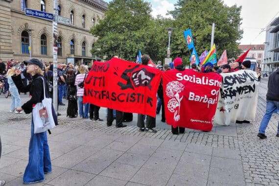 Linke Protest-Demo am Magdeburger Hauptbahnhof mit Bannern „Sozialismus oder Barbarei“; Polizei im Einsatz.