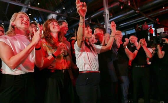 Linken-Wahlparty in Berlin: Menschen jubeln, Scheinwerfer und Partyatmosphäre, im Kontext Vergesellschaftungsdebatte.