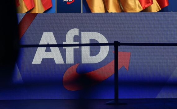 AfD-Logo (Archiv) vor Warnkulisse: Ökonomen befürchten wirtschaftlichen Schaden bei AfD-Regierungsübernahmen.