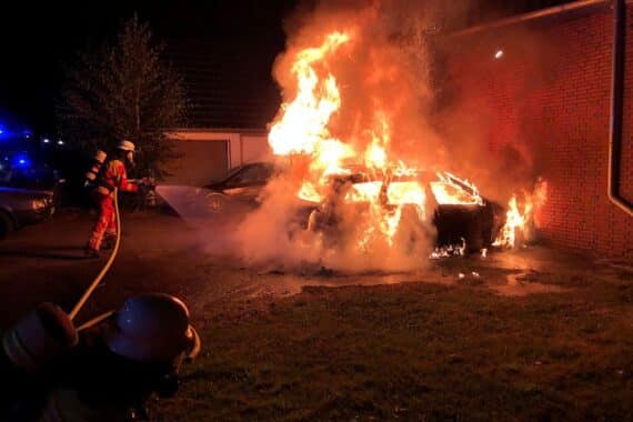 Brennender PKW direkt vor einer Haustür, Einsatzkräfte der Feuerwehr, Löscharbeiten am Wohnhaus (Archiv).