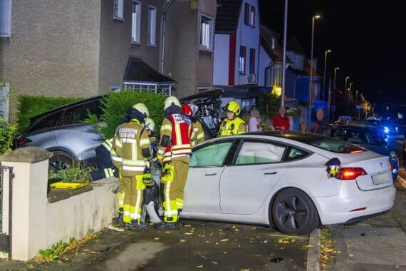 Verkehrsunfall in Iserlohn: beschädigter Tesla kollidiert mit drei geparkten Autos, Feuerwehr am Einsatzort.