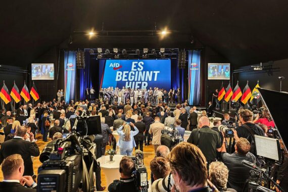 AfD-Wahlparty in Jena, 06.09.2026: Parteifans feiern, Politiker sprechen, Bild zeigt rechtspopulistische Stimmung.