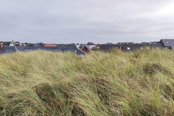 Wolkenverhangene Häuser auf Sylt, im Hintergrund Küste und Regen—zeitweise wechselhaftes Norddeutschland, Archivfoto.