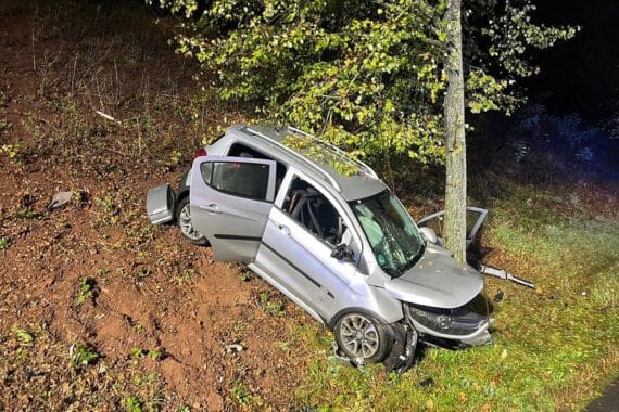Verunfallter Opel im Grünstreifen, regennasse Straße, Rettungswagen, Polizei bei Verkehrsabsicherung.