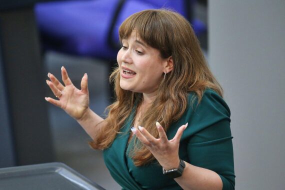 Ricarda Lang bei einem politischen Auftritt, im Hintergrund das Logo der Grünen.