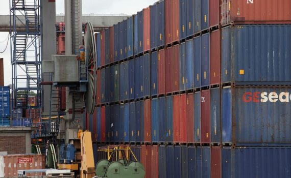 Gestapelte Frachtcontainer in einem Hafen als Symbol für Warenhandel und steigende Importpreise.