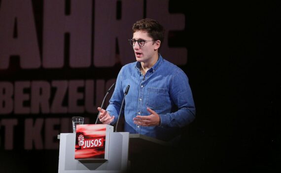 Juso-Chef Philipp Türmer bei einer Rede vor rotem Hintergrund mit SPD-Logo.