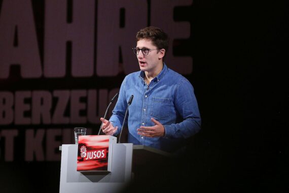 Juso-Chef Philipp Türmer bei einer Rede vor rotem Hintergrund mit SPD-Logo.