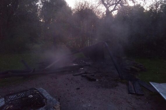 Feuerwehr und Polizei am Brandort in Bad Bramstedt; brennender Altkleidercontainer und abgebrannter Grillunterstand.