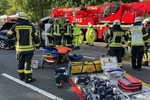 Einsatzkräfte sichern eine Unfallstelle im Bonner Zentrum, befreien eine unter einem Auto eingeklemmte Person.