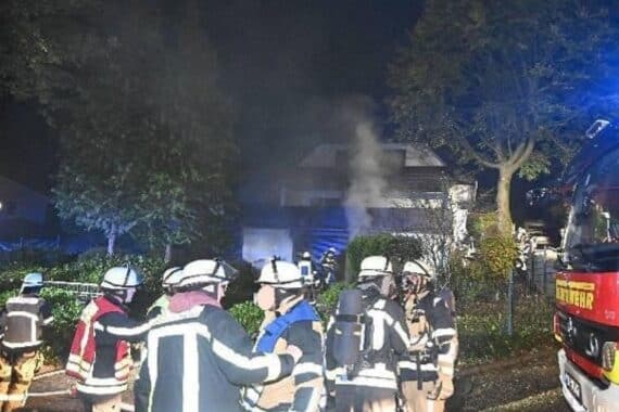 Rauch dringt aus der Garage eines Einfamilienhauses; Feuerwehr und Polizei vor dem Haus.