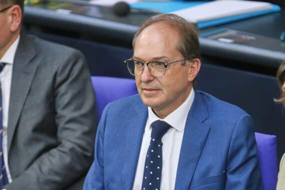 Alexander Dobrindt im Porträt, dahinter Berliner Wohnhäuser als Symbol für den Streit um Vergesellschaftungen.