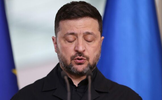 Wolodymyr Selenskyj im Archivfoto, Donald Trump im Hintergrund: US-Kritik und Ablösungsforderung.